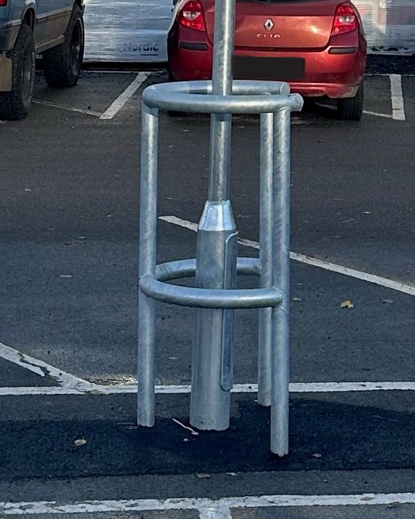 A horseshoe-shaped column protector is installed around a lamppost in a parking lot.